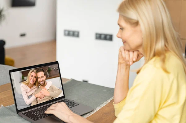 Επιστροφή δείτε μια ηλικιωμένη γυναίκα χρησιμοποιώντας ένα φορητό υπολογιστή για βιντεοκλήση. Μια ηλικιωμένη μητέρα μιλάει στο διαδίκτυο με μια ενήλικη κόρη και τον άντρα της, βιντεοσυνάντηση με μια οικογένεια. — Φωτογραφία Αρχείου