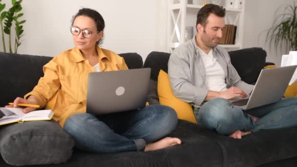 Para używająca laptopów do zdalnej pracy na sofie w domu, skupieni małżonkowie pracujący na odległość — Wideo stockowe