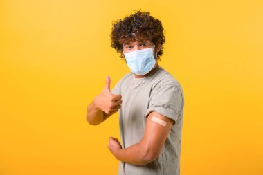 Tıbbi maskeli kıvırcık saçlı adam iğne oldu ve kolunda yama var.