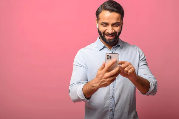 Smiling Indian man holding and using smartphone, carefree multiracial guy enjoying online chatting — Stock fotografie