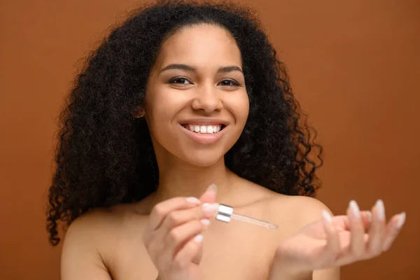 Mujer joven afroamericana glamurosa que usa productos para el cuidado de la piel con gotero — Foto de Stock