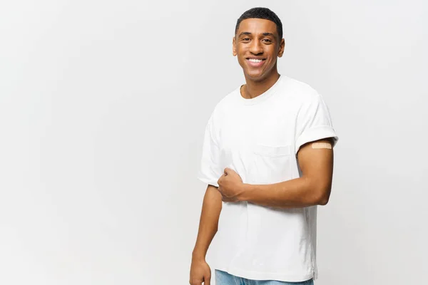 Portrait of happy young African American guy showing arm with patch-aid after coronavirus vaccine — Stok fotoğraf