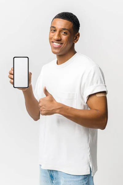 Латиноамериканец с пластырем на руке показывает смартфон с пустым экраном и большим пальцем вверх — стоковое фото