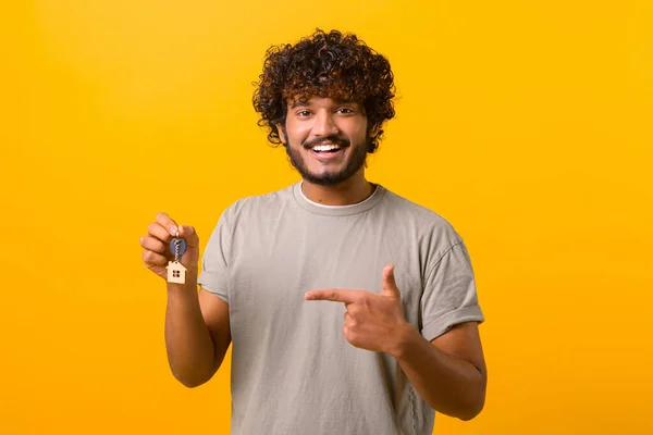 Feliz joven indio mostrando las llaves y el dedo en él de pie aislado en amarillo —  Fotos de Stock