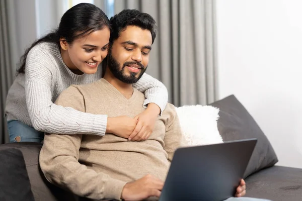 Весела пара закоханих проводить дозвілля онлайн з ноутбуком вдома. Молода жінка і чоловік дивиться на екран ноутбука, сидячи на дивані, дивиться комедійні фільми — стокове фото