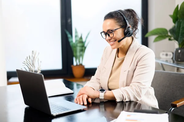 Charming middle-aged business woman, teacher, online tutor wearing headset using laptop for video conference, teaching online, conducts webinar sitting in the office — Foto de Stock
