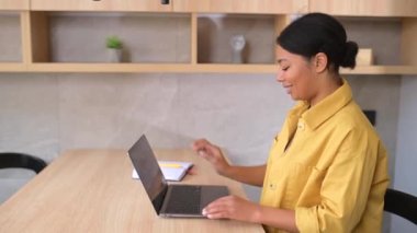 Mutfakta dizüstü bilgisayarla masada oturan, gülümseyen, çok ırklı genç bayan girişimci.