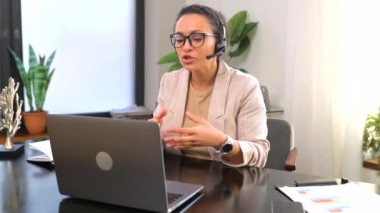 Gülümseyen kadın çağrı merkezi çalışanı çevrimiçi iletişim için kulaklık ve laptop kullanıyor.