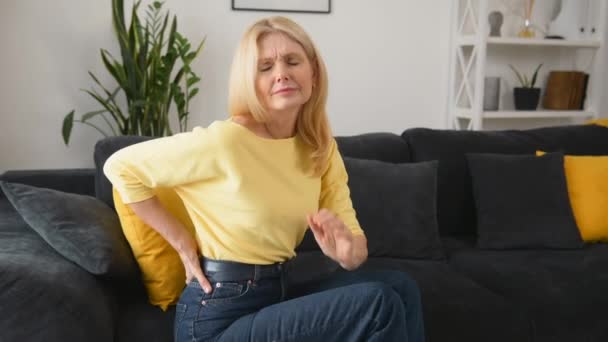 Blonde-haired woman felt a sharp pain in loin sitting on the sofa at home — Stockvideo