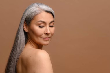 Orta yaşlı, çıplak omuzlu ve uzun gümüş saçlı çekici bir Asyalı kadın portresi.