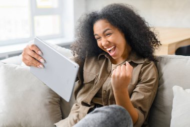 Tablet ekranına bakıp başarıyı kutlayan aşırı neşeli bir kadın. Tablet tutan heyecanlı genç bayan, mesajda iyi haberler okuyor, piyango kazandı.