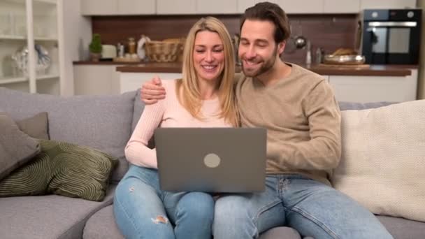 Happy couple using laptop for video connection to friends or family, looking at the webcam — ストック動画