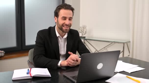 Mosolygó fiatal üzletember formális viselet ül az asztalnál az irodában — Stock videók
