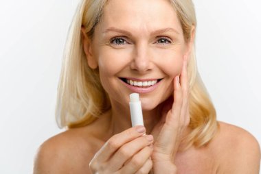 Sarışın kadın nemlendirici ruj ve merhem tutuyor. İyimser, orta yaşlı, doğal dudak kremiyle poz veren, beyaz tenli güzel bir kadın.