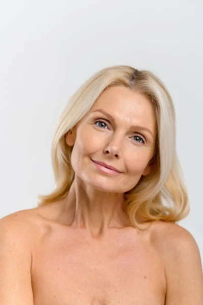 Vertical view of the attractive middle-aged blonde woman looking at the camera over white background — стоковое фото