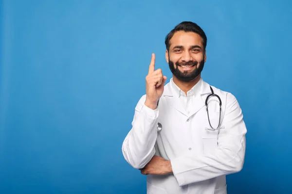 Fiatal indiai férfi orvosi dolgozó fehér köpenyt visel sztetoszkóppal a válla fölött álló elszigetelt kék — Stock Fotó