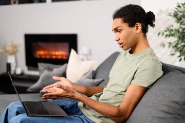 Sanal toplantı, video çağrısı konsepti. Rahat koltukta oturan neşeli, çok kültürlü bir adam interinterinterlocutor ile konuşurken video görüşmesi için son moda dizüstü bilgisayarını kullanıyor.