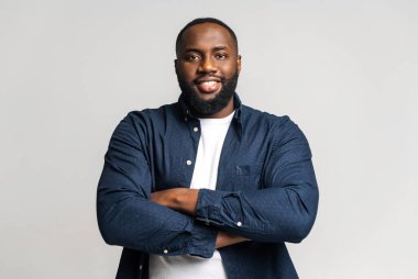 Smiling African-American male employee wearing casual shirt stands with arms crossed
