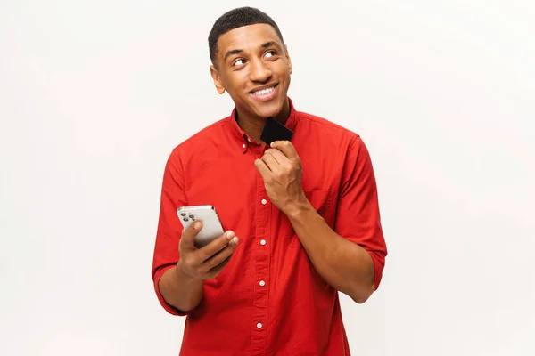Homme afro-américain souriant en chemise rouge isolé sur fond blanc pensant et rêvant d'un achat tant attendu — Photo