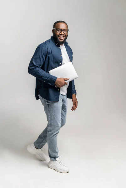 Glada afroamerikanska mannen bär bärbar bärbar dator isolerad på grå — Stockfoto