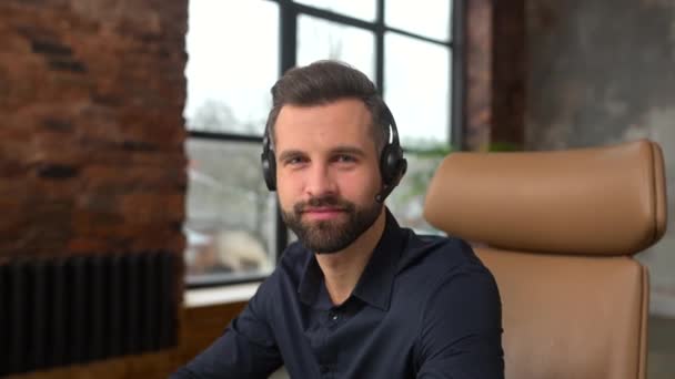 Positivo joven guapo barbudo hombre empleado en auriculares — Vídeos de Stock