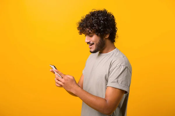 Boční pohled na indiána s kudrnatými vlasy pomocí mobilního telefonu, psaní textové zprávy — Stock fotografie
