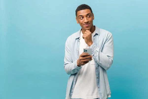 Tankeväckande ung multiracial kortklippt man i ledig skjorta stående med smartphone och hålla haka — Stockfoto