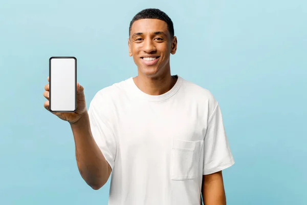 Happy African-American young guy showing phone with empty screen isolated on blue — Stock fotografie
