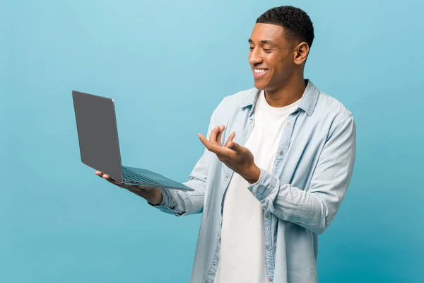 Handsome happy african-american male student in casual jeans shirt using laptop pc for video call — Stock fotografie