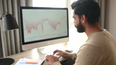Uzak işlerde bilgisayar kullanan Hintli erkek tüccar kripto para birimi finansal piyasa analizi yapıyor.