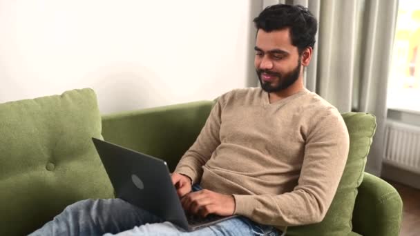 Hombre optimista acostado en el sofá y el uso de ordenador portátil para la mensajería — Vídeo de stock