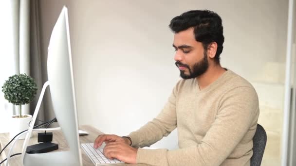 Оптимістична етнічна людина в повсякденному одязі за допомогою комп'ютера, що сидить за столом — стокове відео
