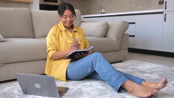 Calm African-American woman sits on the floor in cozy living room with a laptop — Stockvideo