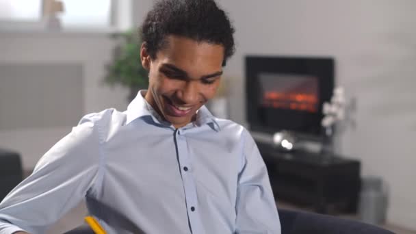 Multiracial guy watching webinar, taking educational course online, while sitting on couch at home — Stockvideo