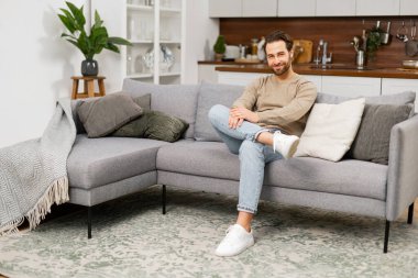 Kanepede dinlenen beyaz bir gencin portresi. Kanepede oturan yakışıklı, pozitif adam. Oturma odasında oturuyor, hayal kuruyor ve dinleniyor.