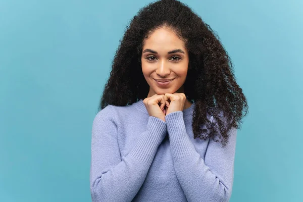 Gorgeous 20s multiracial lady looks at the camera with light smile. Joyful African-American young woman with curly hairstyle wearing stylish sweater isolated — стоковое фото