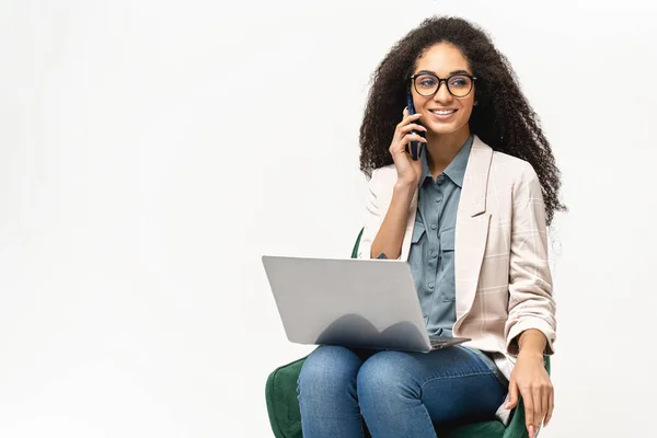 Femme afro-américaine confiante en tenue décontractée intelligente utilisant un ordinateur portable et parlant sur le smartphone isolé sur fond blanc — Photo
