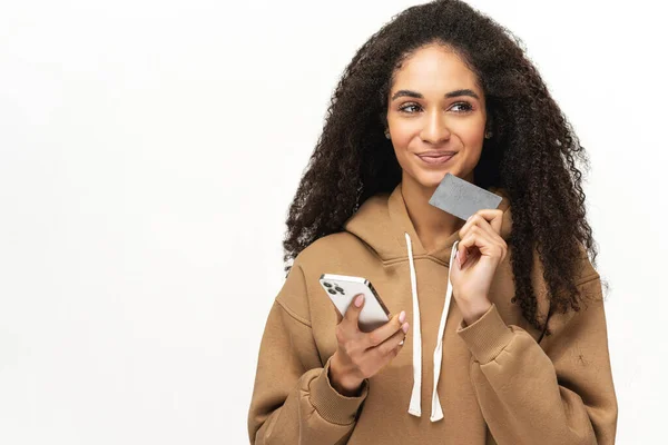 Image of pondering dreaming pretty woman posing isolated over white wall background using phone holding credit card — стоковое фото