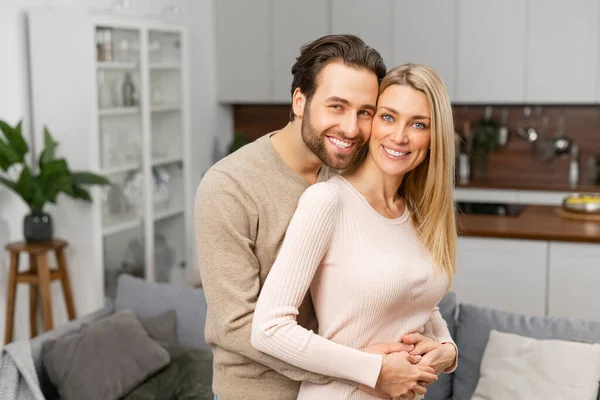 Happy married couple posing for a photo on kitchen. Happiest hearts make the happiest homes, caucasian husband hugging his wife from behind — Foto Stock