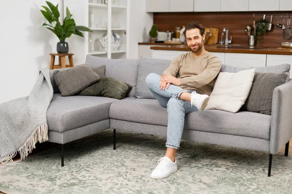 Kanepede dinlenen beyaz bir gencin portresi. Kanepede oturan yakışıklı, pozitif adam. Oturma odasında oturuyor, hayal kuruyor ve dinleniyor.