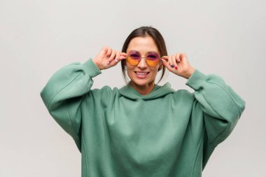 Gülümseyen, güneş gözlüklü güzel Asyalı kızın portresi beyaz arka planda mutlu bir ifadeyle poz veriyor.