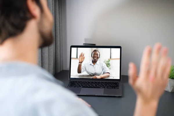 ビデオ接続のためのラップトップコンピュータを使用して陽気な屈託のない男は、ウェブカメラを見て手を振って。テーブルに座ってビデオ通話をする男 — ストック写真