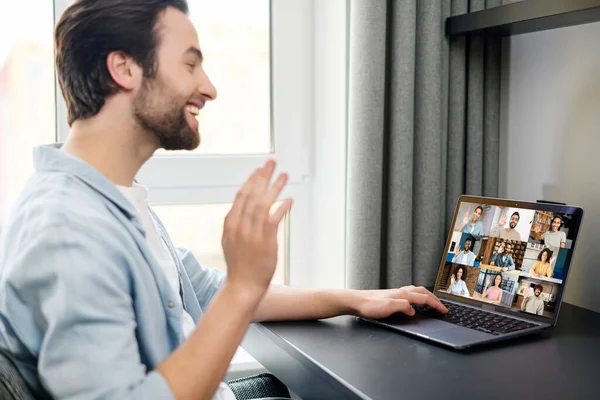 Virtual conference, webinar. Young cheerful caucasian man waves hello to many diverse people on the laptop — Fotografia de Stock