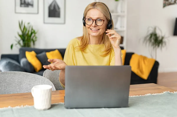 Smiling female call center employee using a headset and laptop for online communication with customers, a woman talking into microphone — стоковое фото