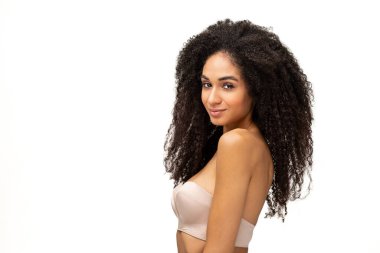 Yakışıklı, çok kültürlü, sutyen takan genç bir kadın kameraya bakıyor ve beyaz arka planda gülümsüyor.