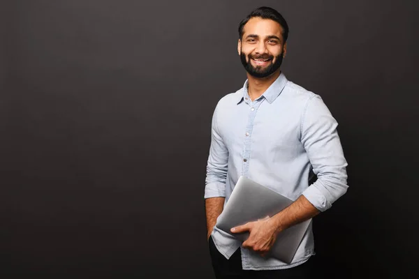Cheerful Indian bearded man holding laptop standing isolated on black — Stock Photo, Image