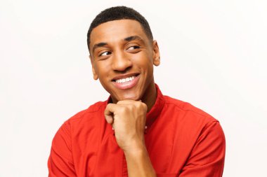 Thoughtful smiling African-American young man in red shirt lost in dreams isolated on white
