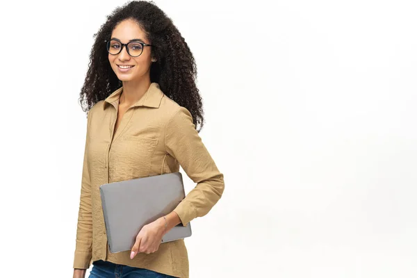 Joven mujer afroamericana con peinado afro que usa ropa casual inteligente y anteojos elegantes de pie aislados en blanco, portando computadora portátil, sonriente, empleada de oficina femenina — Foto de Stock