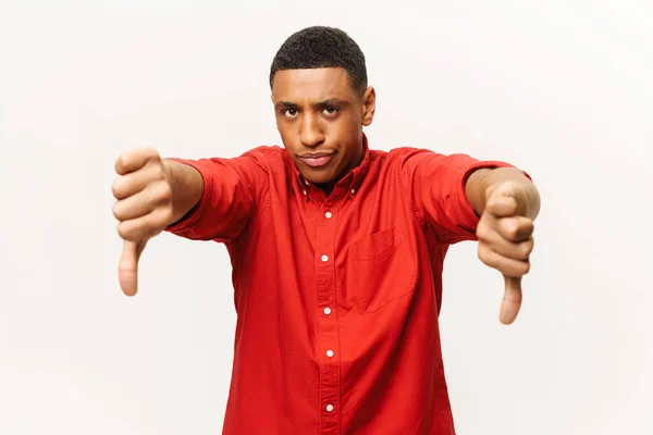 Annoyed African-American young man in red casual shirt showing thumb down, expresses disagreement with grimace on the face — Fotografia de Stock