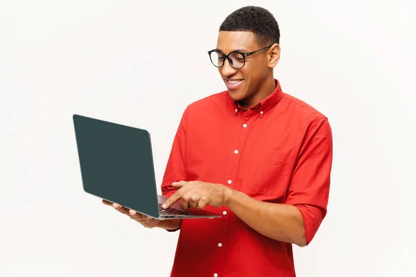 Cheerful handsome smiling African-American young man in red shirt using laptop isolated on white — Stock fotografie
